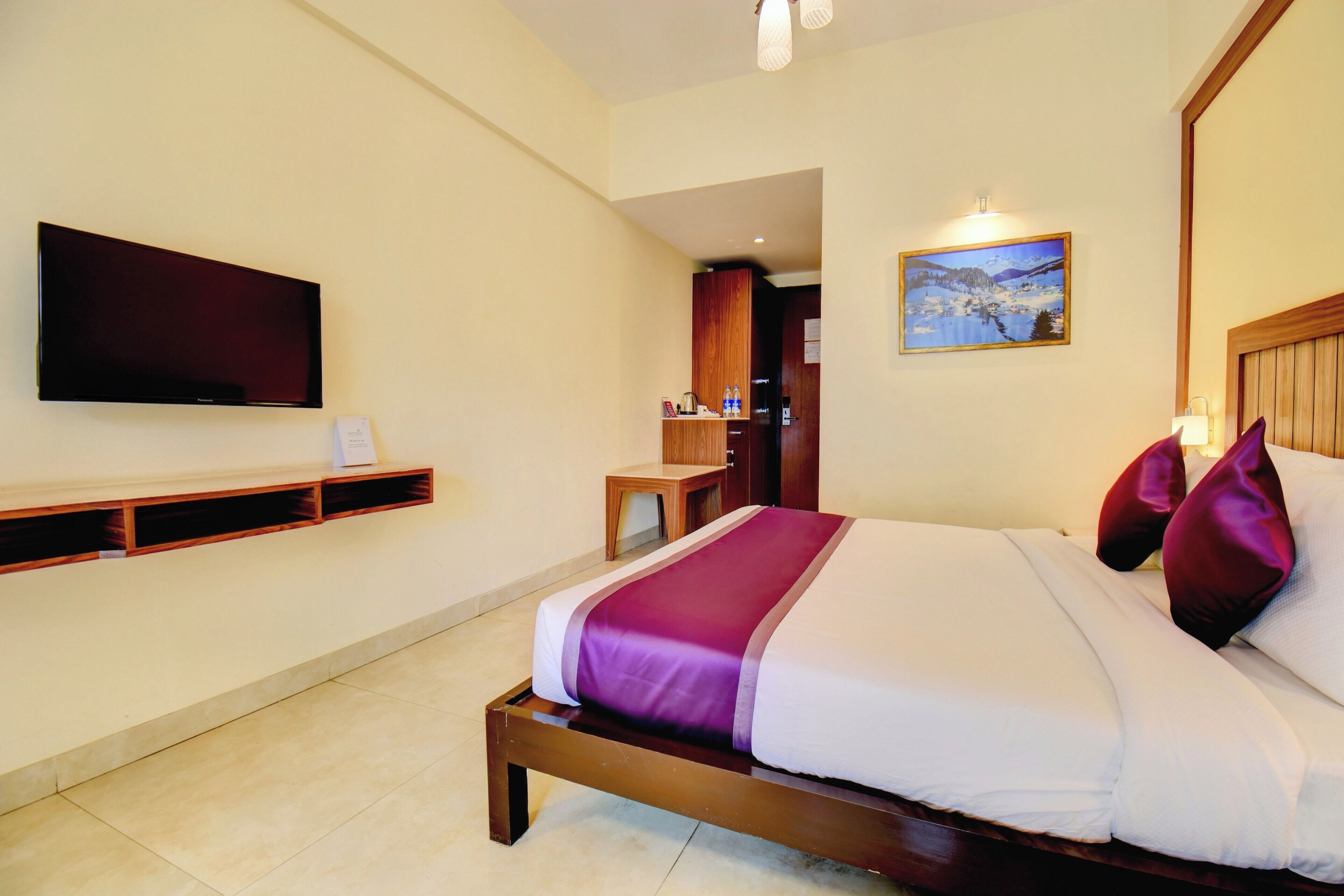 Una habitación de hotel con cama, televisión montada en la pared, un cuadro y cabecera de madera.