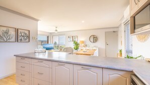 A modern kitchen with a large island, a dining area with a table and chairs, and a view of the outdoors. - Commodore 6, 6 Intrepid Cl - water views, Air Con, Wi-Fi (Nelson Bay)
