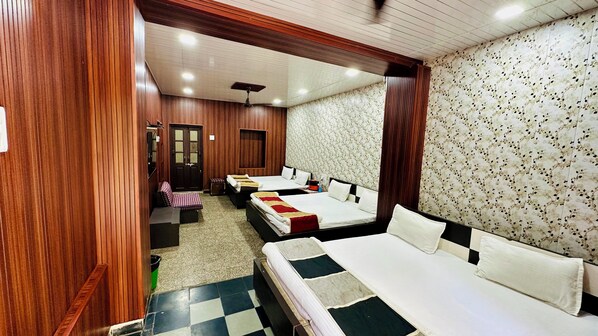 A hotel room with three beds, wooden paneling, floral wallpaper, and a checkered floor.