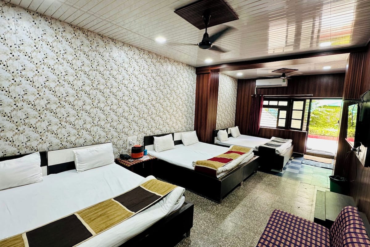 A hotel room with two beds, a TV, and a window with a view of greenery.