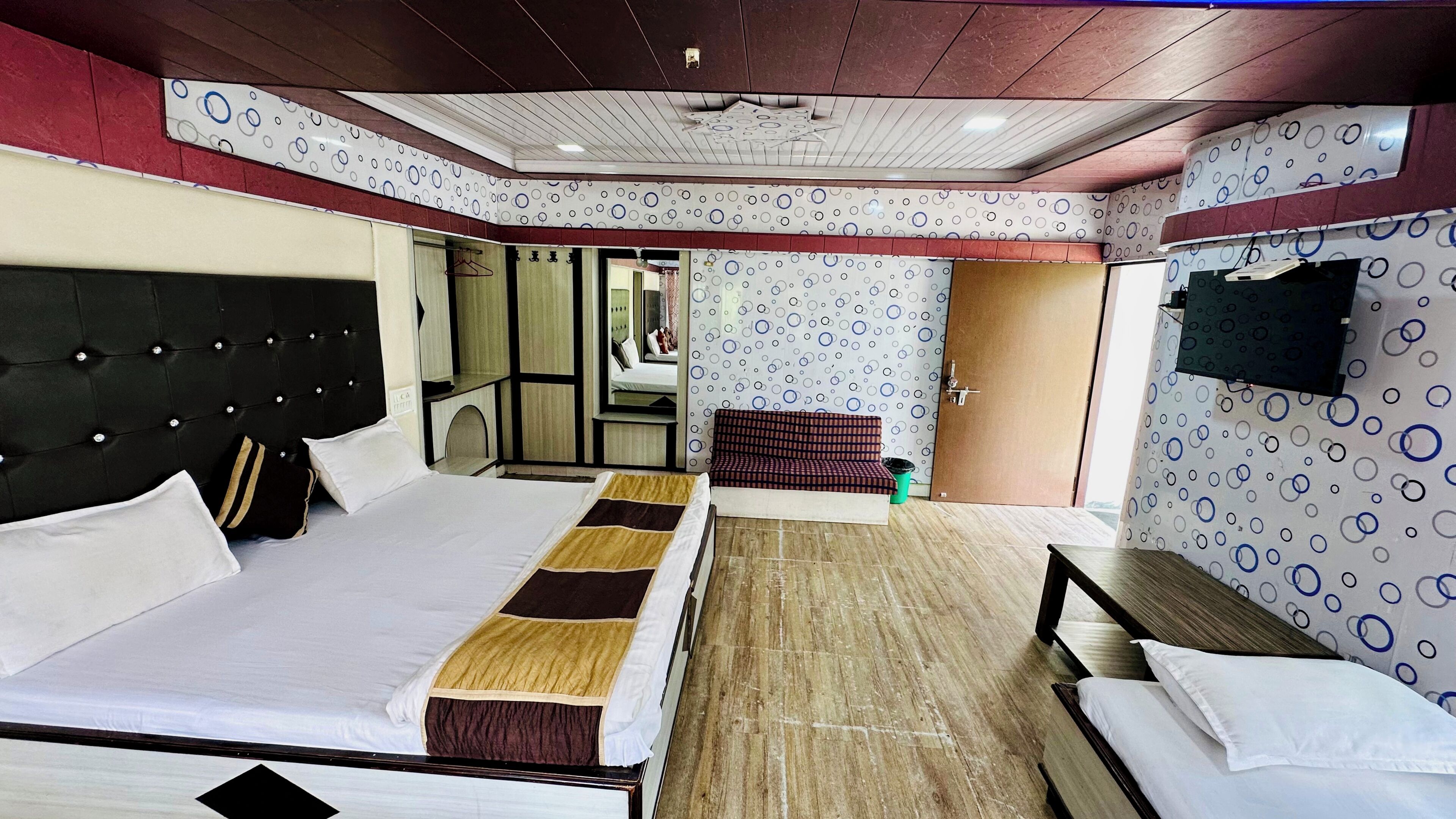 A hotel room with a large bed, a smaller bed, a sofa, and a TV mounted on the wall.