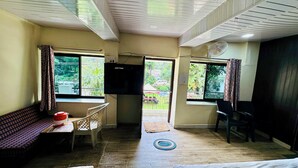 Ein Zimmer mit einer Couch, einem Tisch mit einem roten Topf, einem an der Wand montierten Fernseher und einem Deckenventilator.
