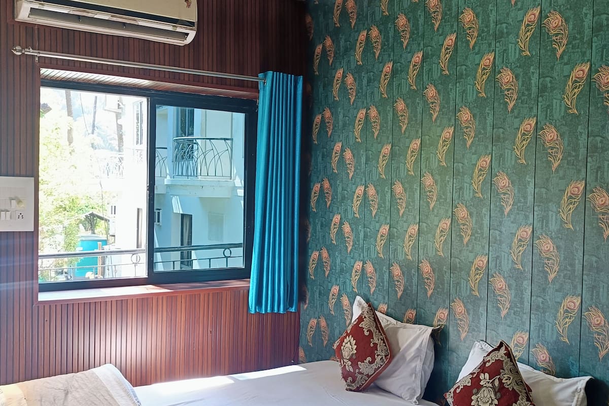 A hotel room with a large bed, a window with curtains, a patterned wall, and an air conditioning unit.