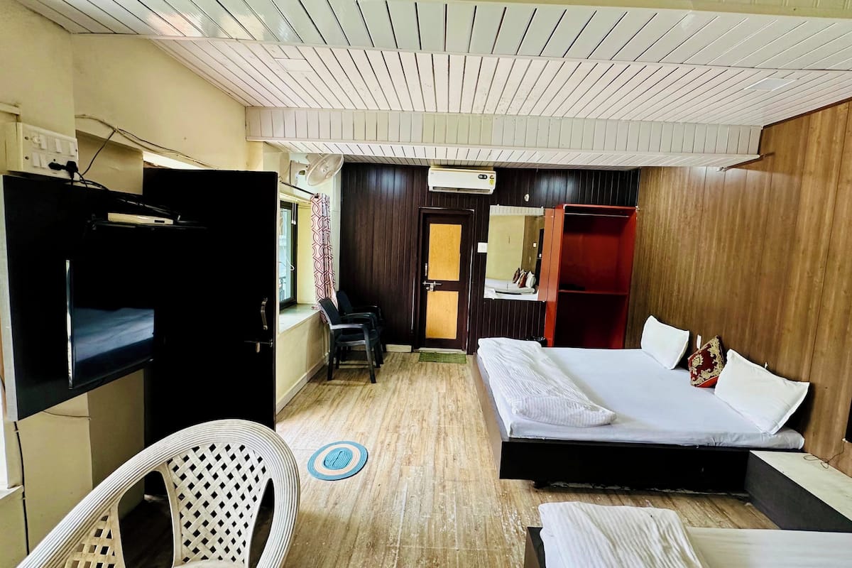 A hotel room with a bed, a desk, a chair, a wardrobe, and an air conditioning unit.