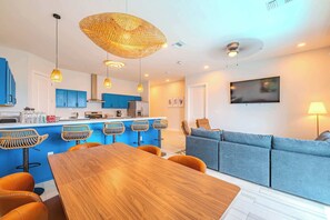 A modern kitchen with blue cabinets, a wooden dining table, and a bar area with stools.