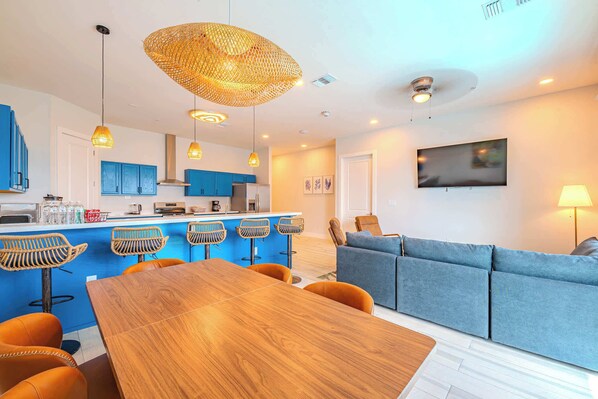 A modern kitchen with blue cabinets, a wooden dining table, and a bar area with stools.