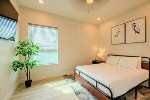 A bedroom with a bed, a potted plant, a window with blinds, and two wall-mounted bird paintings.