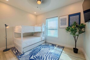 A bedroom with a bunk bed, a floor lamp, a potted plant, and artwork on the wall.