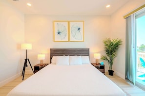 A hotel room with a large bed, two bedside tables with lamps, a potted plant, and artwork on the wall.