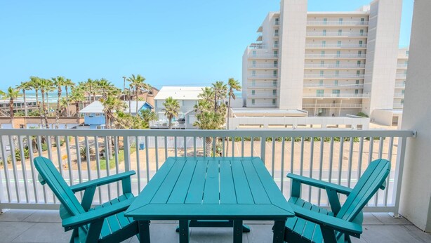 Un balcon avec une table et des chaises, donnant sur un parking et des immeubles.
