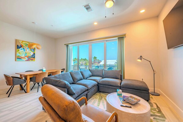 A modern living room with a sectional sofa, a round coffee table, and a dining area with a wooden table and chairs.