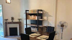 A dining area with a wooden table set for four, black chairs, a bookshelf with books, a fireplace, and a standing fan. - Beautiful House - 15 min from Paris Center (Deuil-la-Barre)