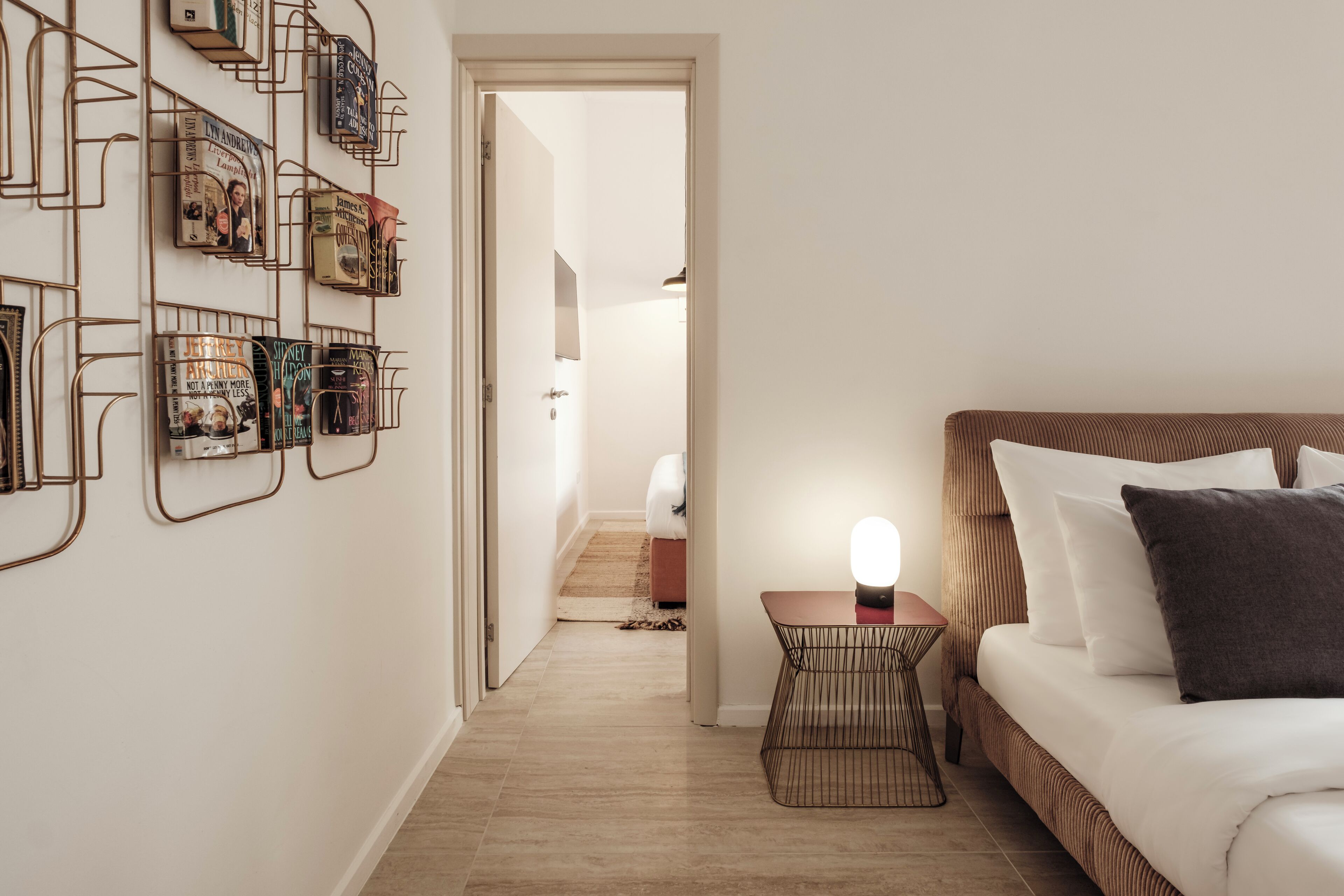 A bedroom with a bed, bedside table, and a wall-mounted book rack.