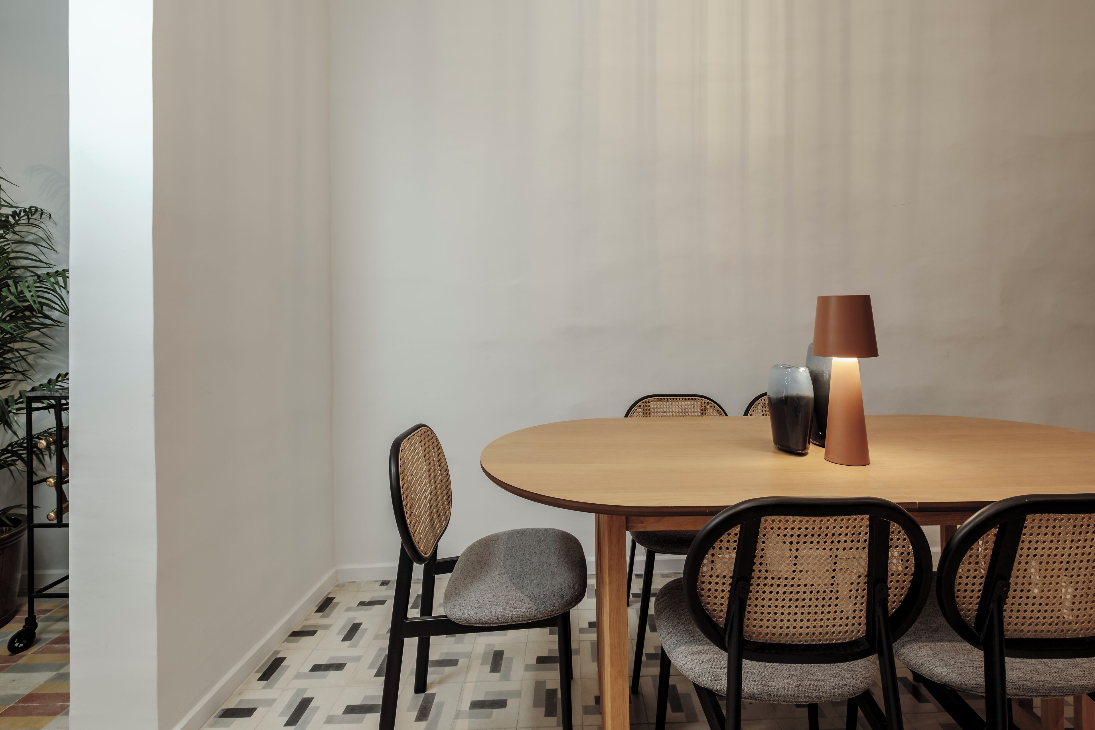 A dining area with a round wooden table, four chairs with cushioned seats, and a table lamp.
