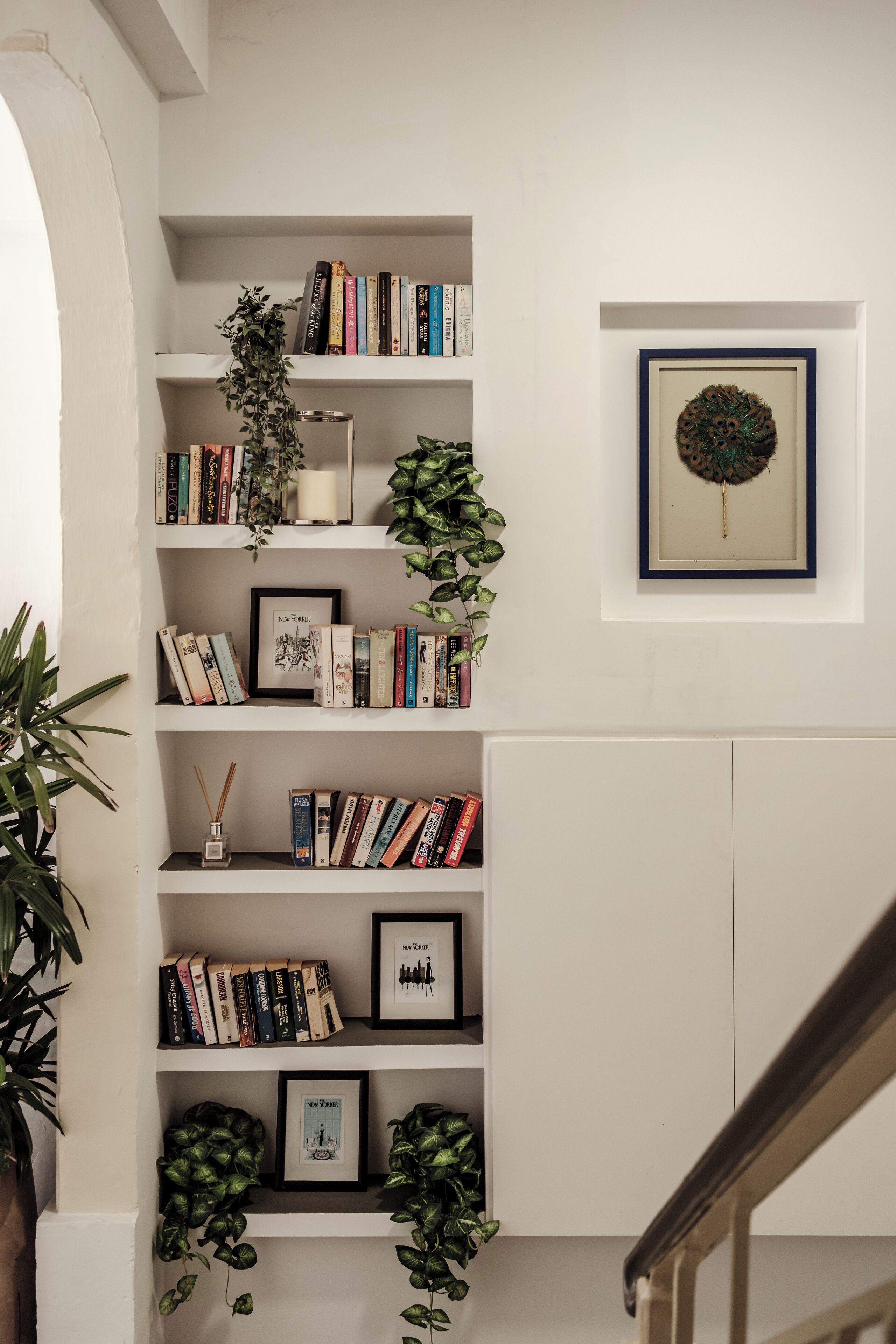 Una estantería con libros y fotografías enmarcadas, una planta en maceta y una obra de arte en la pared.