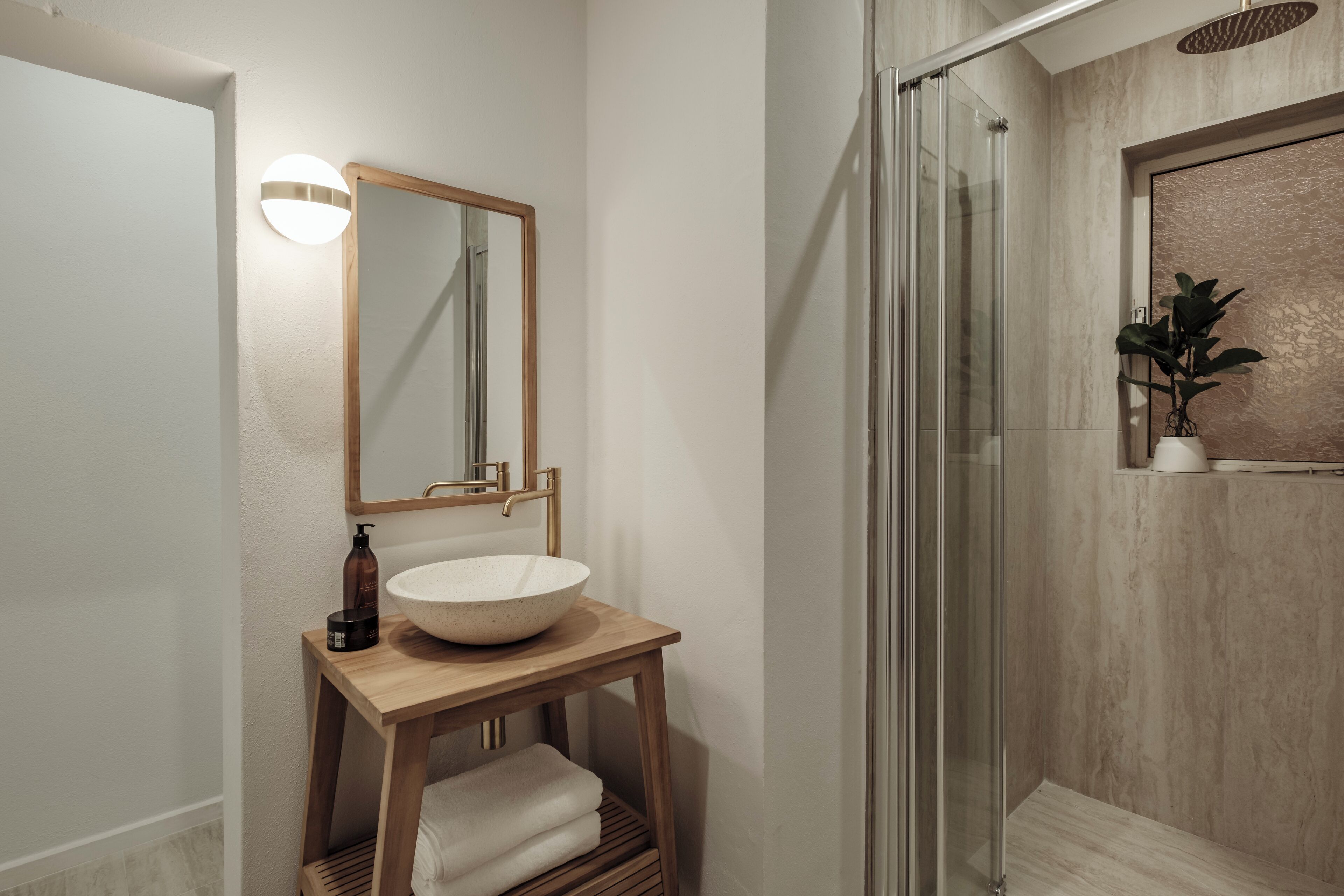 A modern bathroom with a wooden vanity, a large mirror, and a glass shower enclosure.