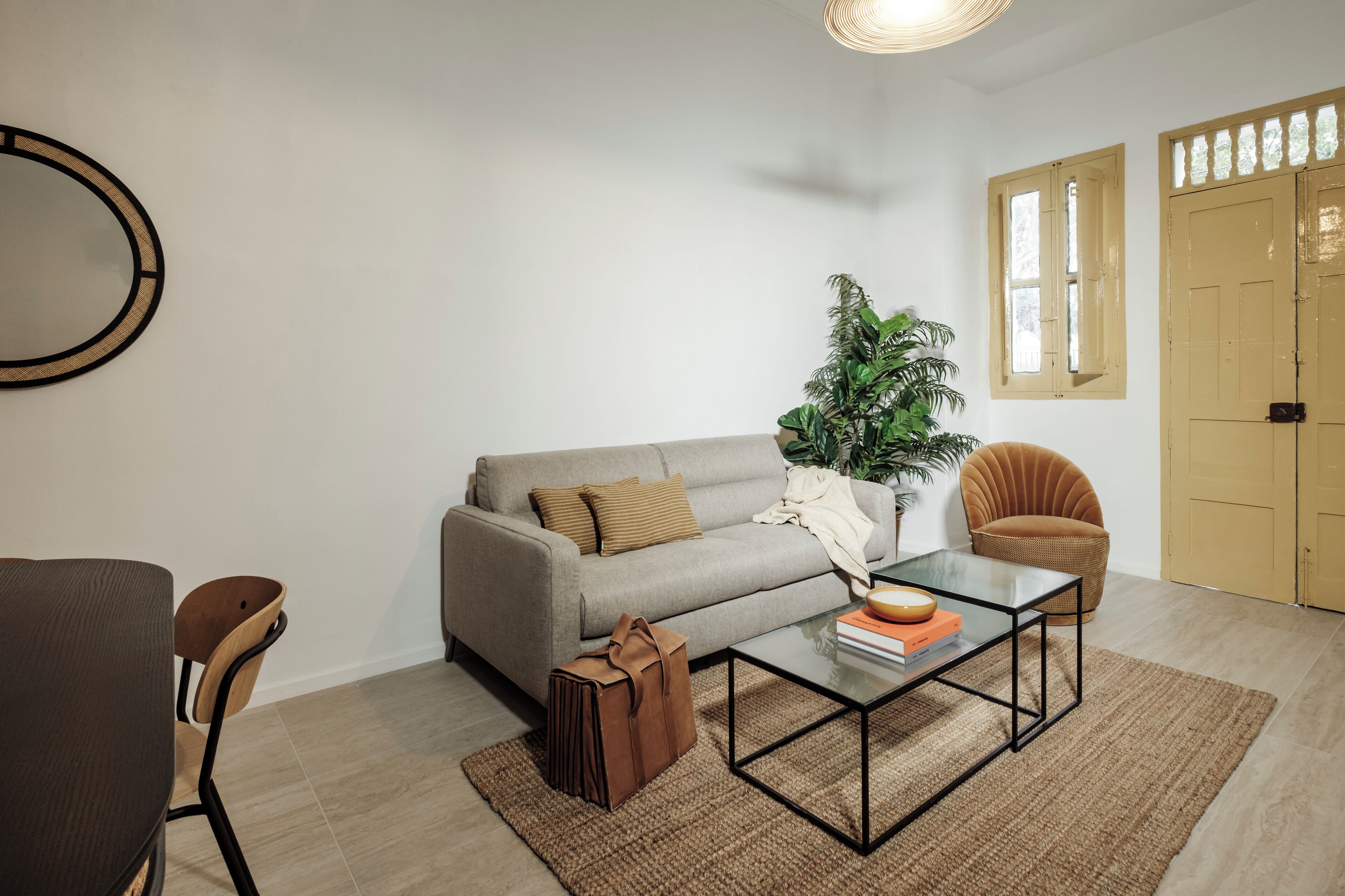 A living room with a sofa, a coffee table, a chair, a plant, and a door.