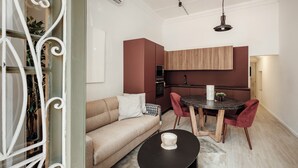 A modern kitchen with a dining area, featuring a round table, red chairs, and a beige sofa. - Ellul Living (Floriana)