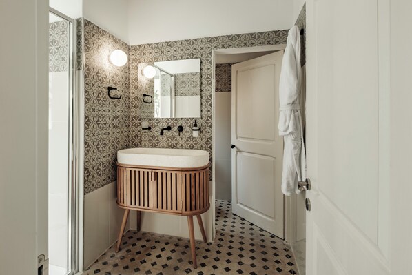 A bathroom with a wooden vanity, a mirror, and patterned wallpaper. - Ellul Living (Floriana)