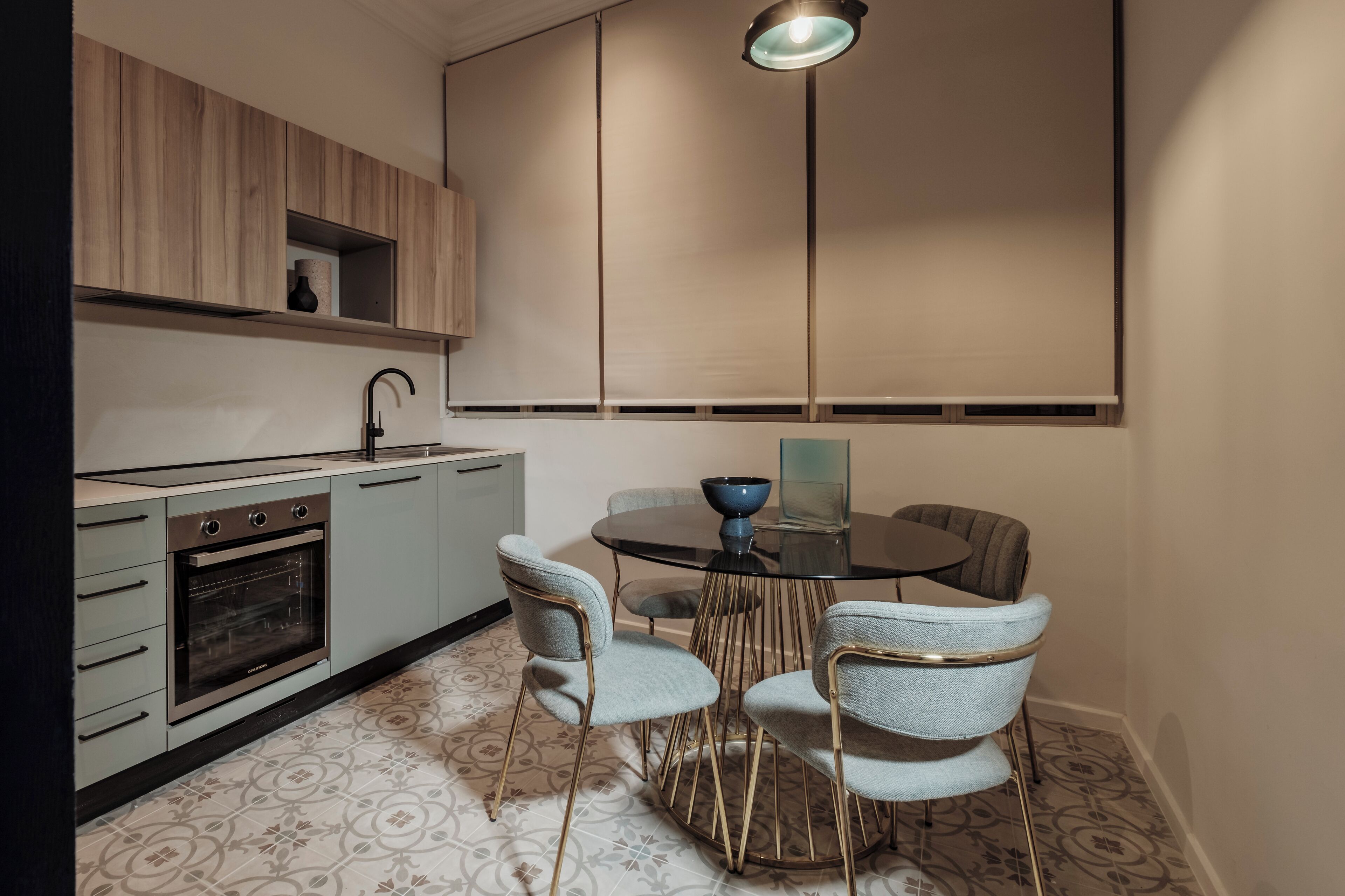 A modern kitchen with a built-in oven, a dining table with four chairs, and a pendant light.