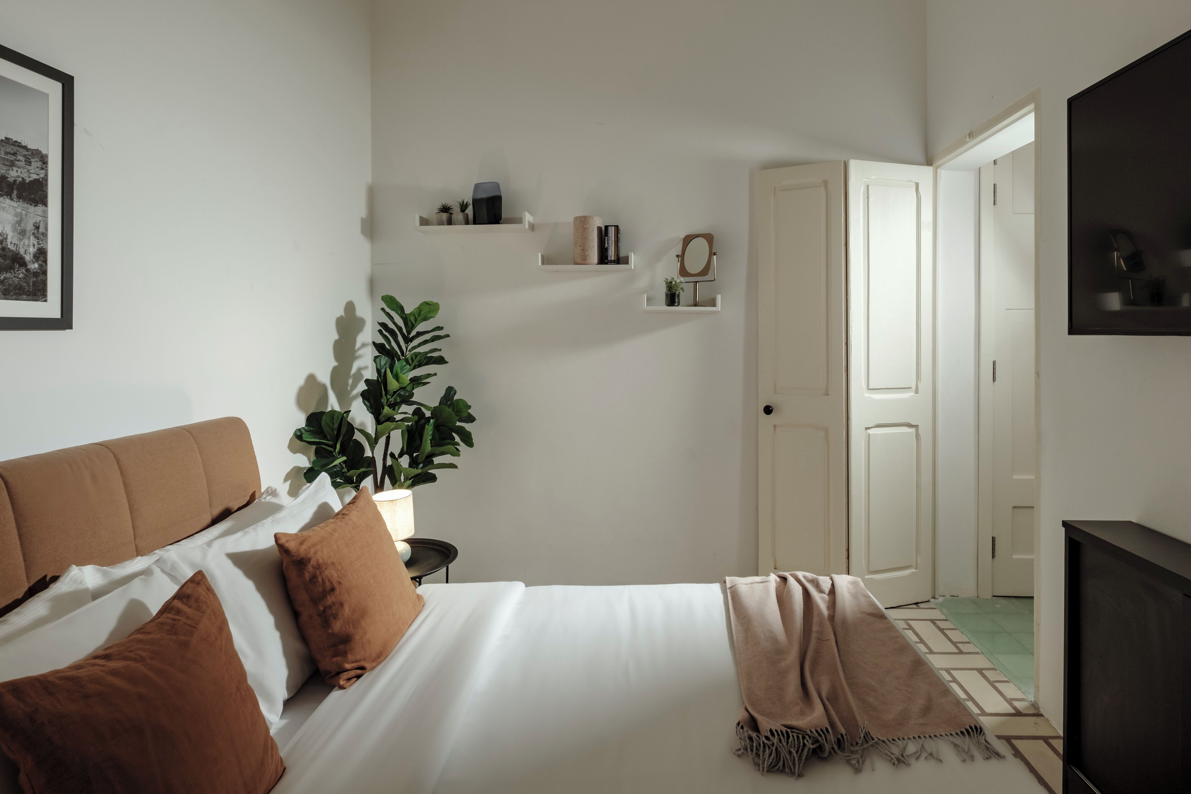 Ein Schlafzimmer mit einem Bett, Kissen, einer Pflanze, einem Spiegel und einem Fernseher.