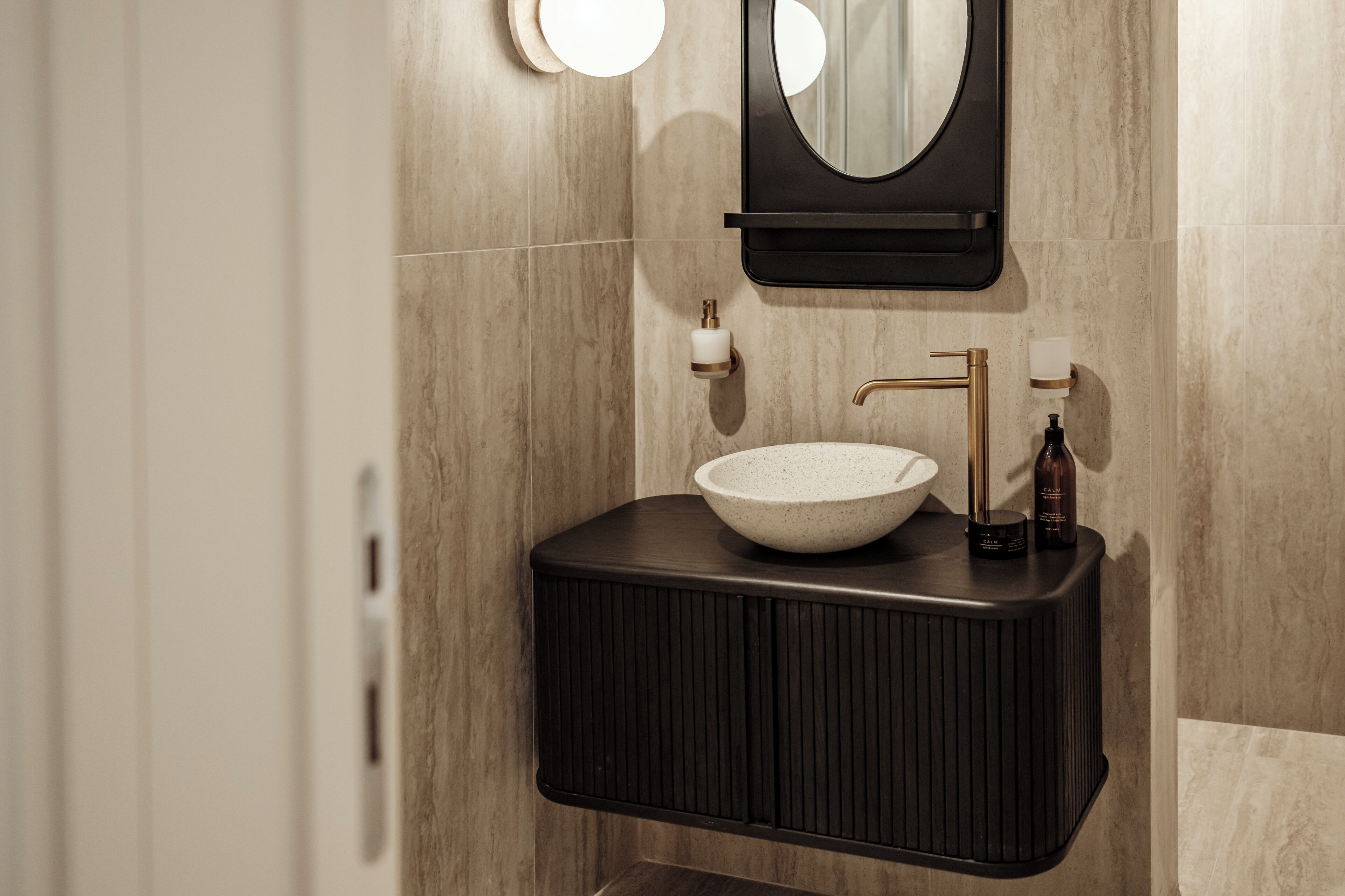 Un baño moderno con un lavamanos sobre encimera, un mueble de tocador negro, un grifo dorado y un espejo redondo.