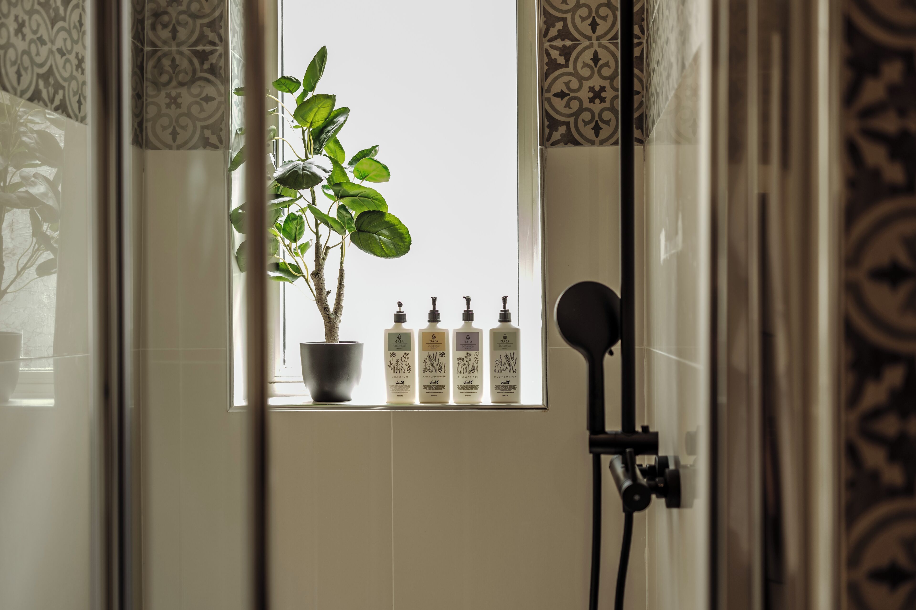 Un baño con ventana, una planta en maceta y cuatro botellas de jabón líquido.