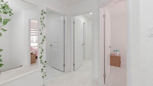 A hallway with white walls and doors leading to bedrooms. There is a plant with green leaves on the left wall. - Amazing Home Niagara Fall .  (Thorold)