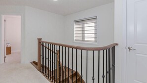 A hallway with a wooden staircase, a white door, and a window with blinds. - Amazing Home Niagara Fall .  (Thorold)