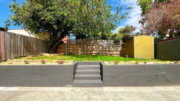 A backyard with a wooden fence, a tree, a shed, and a concrete pathway.
