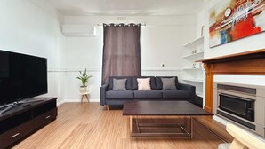 Un salon moderne avec un téléviseur à écran plat, un canapé sombre agrémenté de coussins, une table basse, une cheminée et une plante en pot.