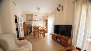 A living room with a sofa, TV, wooden cabinet, and dining area with chairs and a table. - Villa Sueños (Córdoba)