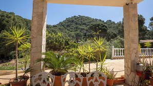 A covered outdoor area with stone columns, potted plants, and a view of a forested hill. - Villa Sueños (Córdoba)