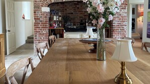 A dining area with a brick fireplace, wooden table, chairs, a vase with flowers, and a lamp. - Eclectic Dorset Country House, Hot Tub, Pool Table, Movie Room,12 guests & pets (Mapperton)