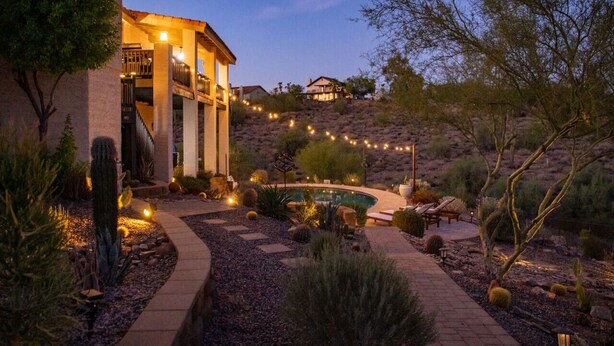 A desert-style house with a swimming pool, surrounded by cacti and desert plants, and string lights in the evening.