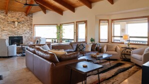 A spacious living room with a stone fireplace, leather sofas, and large windows offering views of the outdoors.