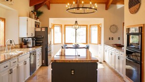 A spacious kitchen with a central island, wooden ceiling beams, and large windows providing natural light.