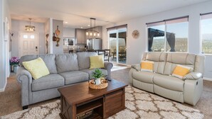 A spacious living area with a grey sofa, a beige sofa, and a wooden coffee table. There is a kitchen in the background, a sliding glass door leading to a balcony, and a ceiling fan. - Hilltop Paradise with stunning views/hot tub/firepit/dog friendly! (Oakhurst)