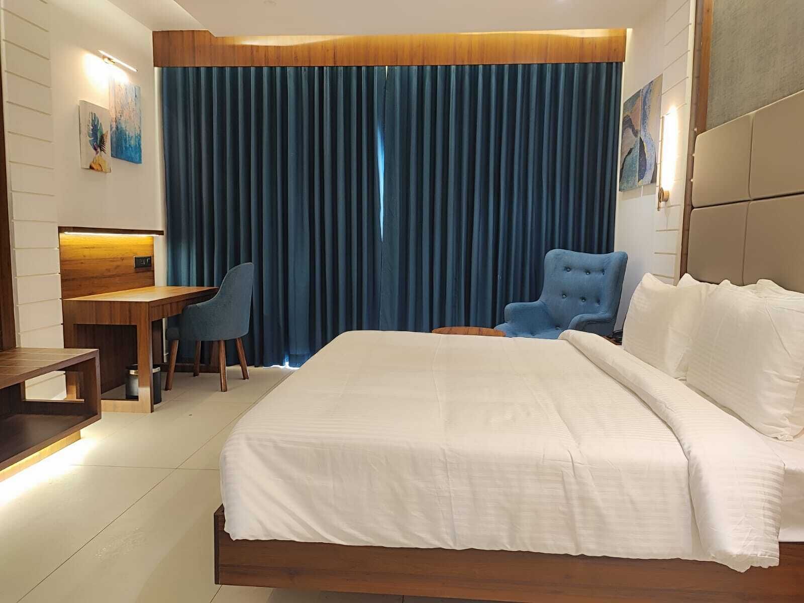 A hotel room with a large bed, a desk, two chairs, and a blue curtain.
