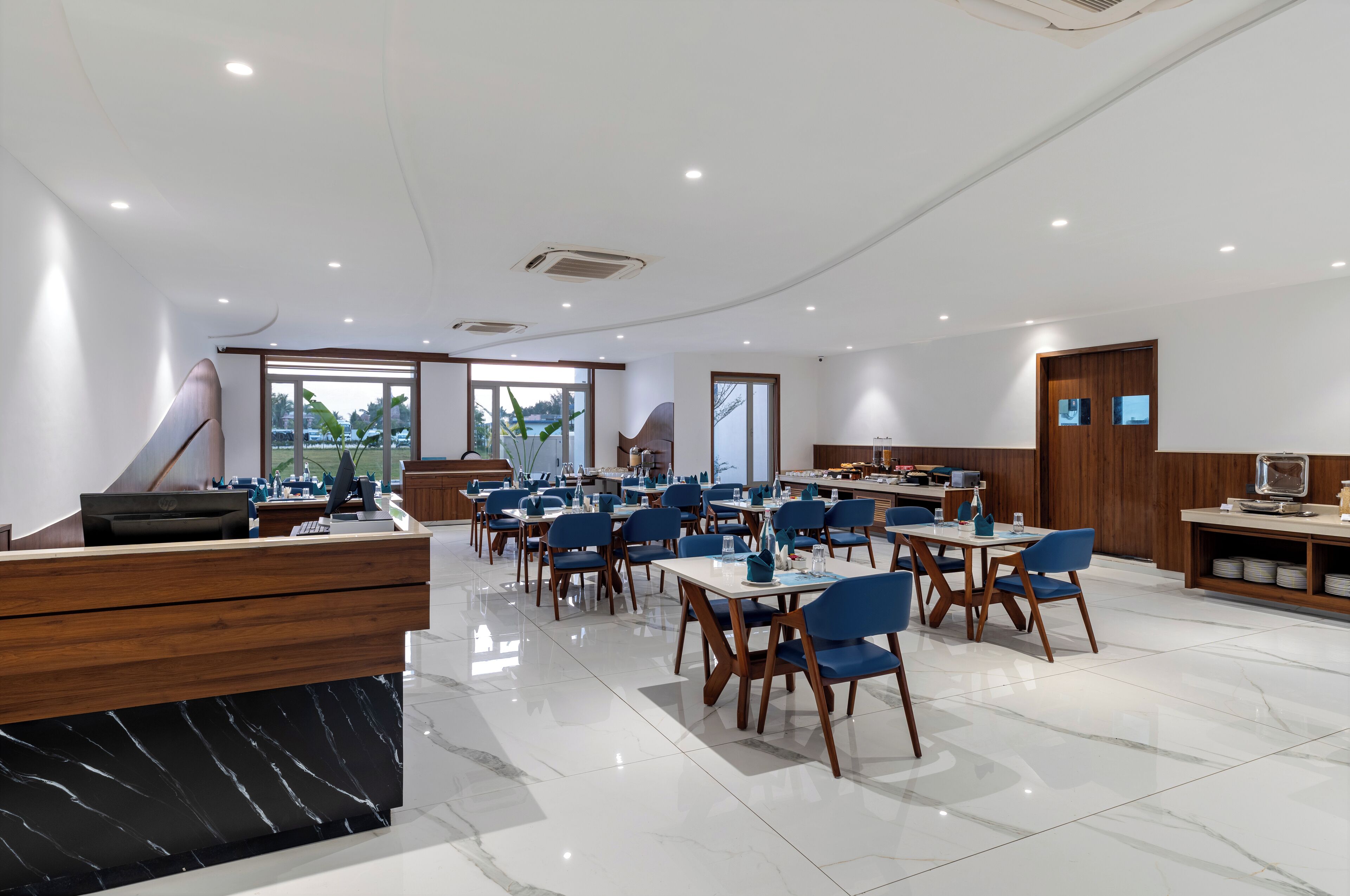 A modern hotel lobby with a reception desk, seating area, and large windows offering a view of the outdoors.