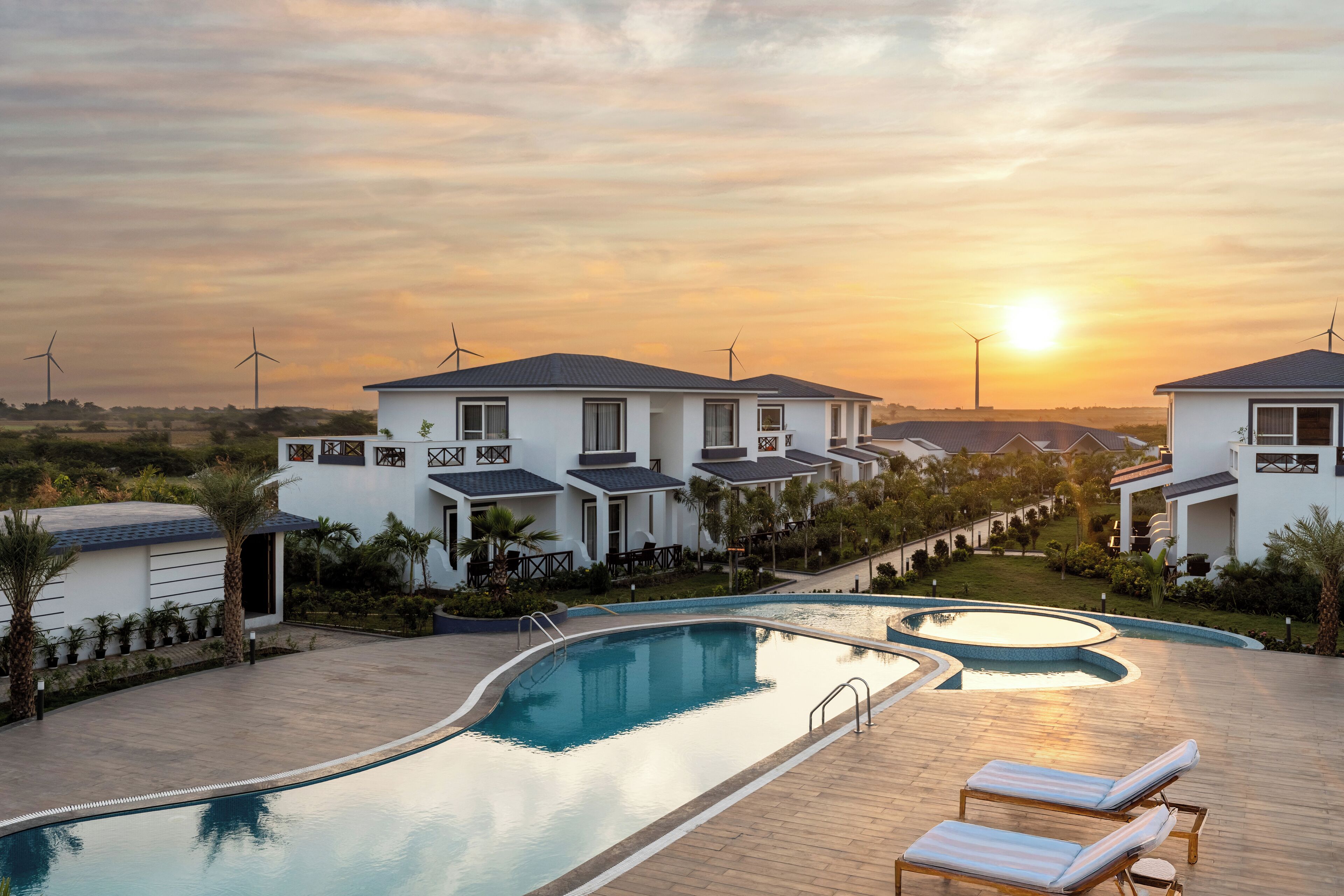 Un resort con piscina, sillas de descanso y aerogeneradores al fondo.