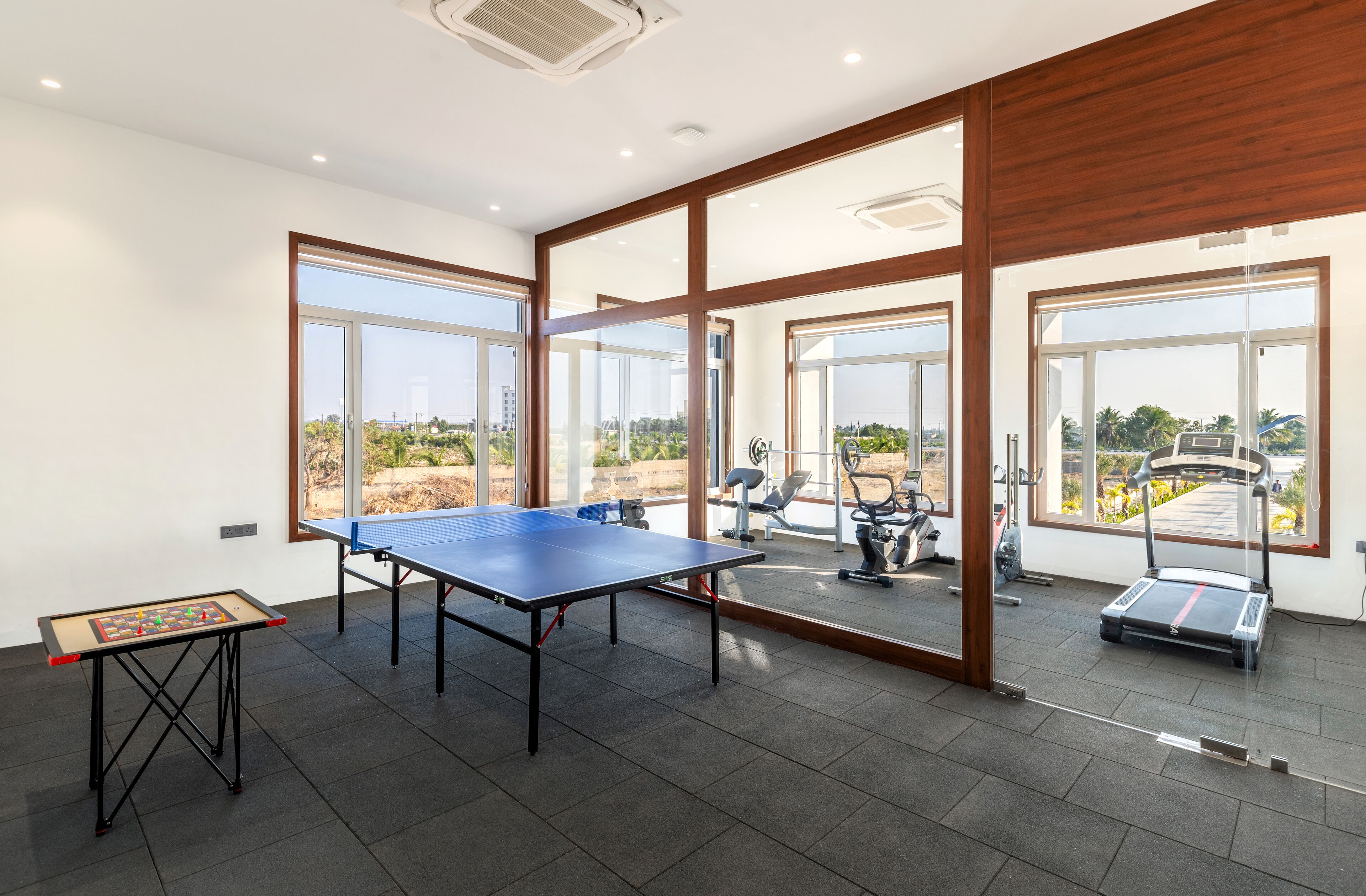 Amplia habitación con mesa de ping pong, equipo de ejercicio y grandes ventanales que ofrecen vistas al exterior.
