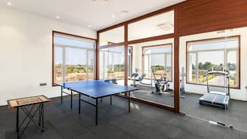 Amplia habitación con mesa de ping pong, equipo de ejercicio y grandes ventanales que ofrecen vistas al exterior.