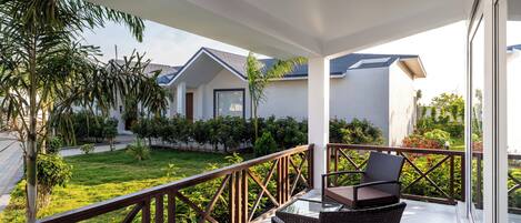 A balcony with wicker furniture, a view of a house, and a well-maintained garden.