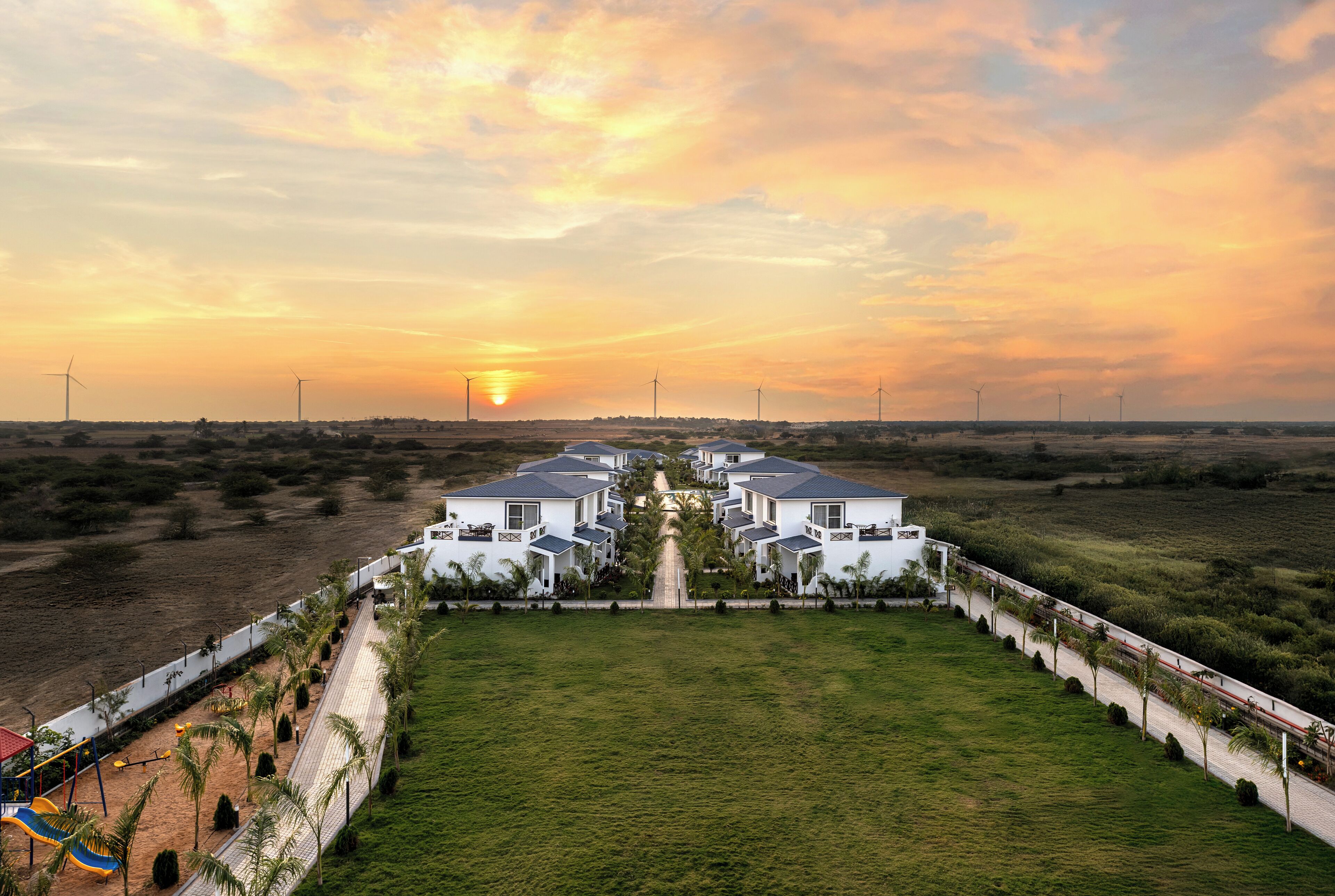 A residential area with a row of white houses, a playground, and a clear view of the sunset.
