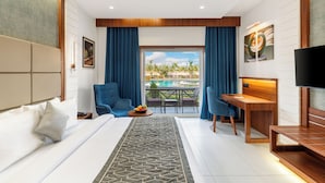 A hotel room with a bed, a desk, a TV, and a balcony with a view of palm trees. - Enrise by Sayaji Dwarka (Dwarka)