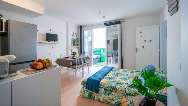 A compact room with a bed, a desk, a kitchenette, and a sliding door leading to a balcony. - Discover the Cocotier Athisien in Athis-Mons, a booming business located 20 minutes from Paris. (Athis-Mons)