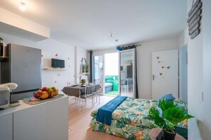 A compact room with a bed, a desk, a kitchenette, and a sliding door leading to a balcony. - Discover the Cocotier Athisien in Athis-Mons, a booming business located 20 minutes from Paris. (Athis-Mons)
