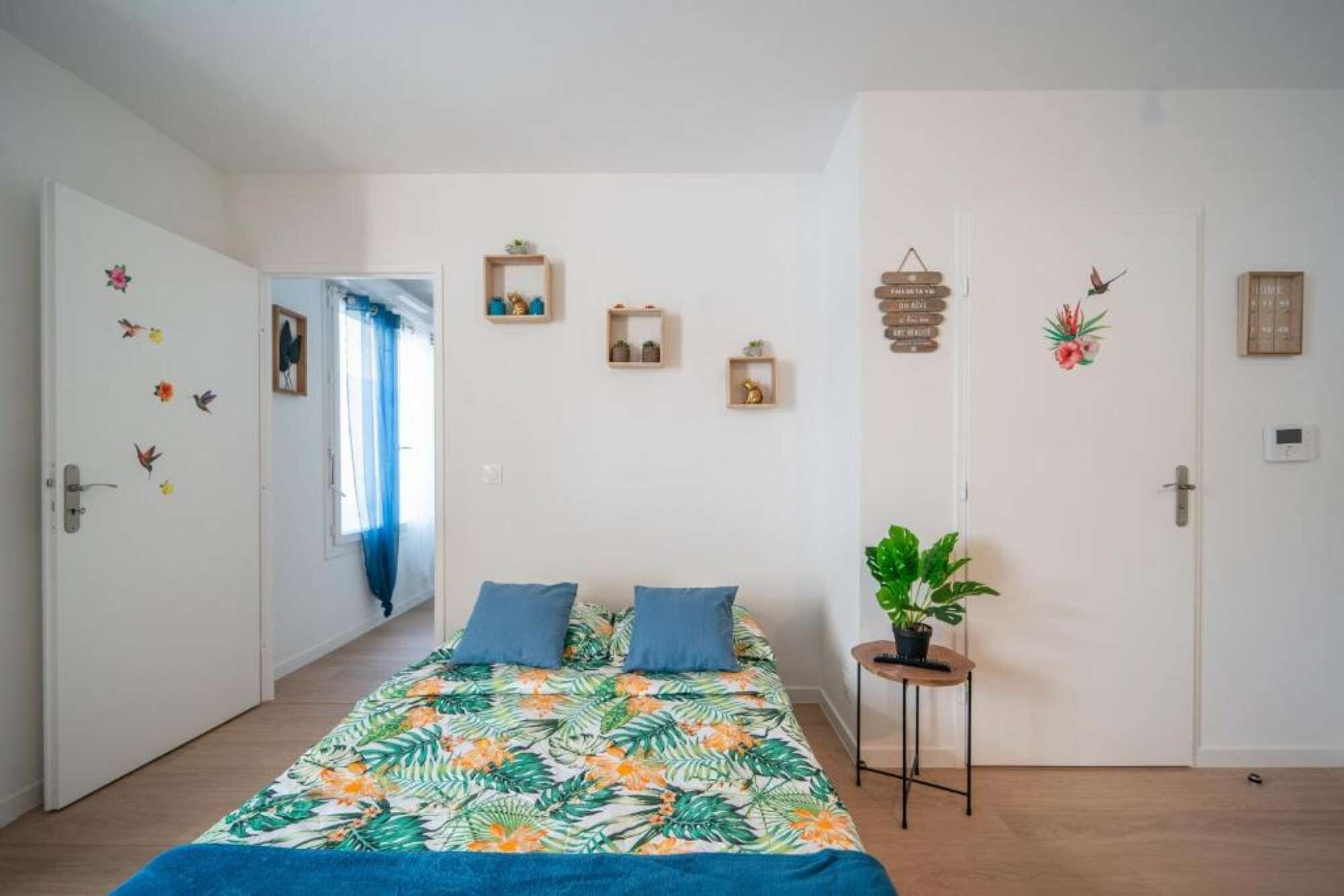 A bedroom with a bed, two pillows, a small table with a plant, and decorative items on the wall.