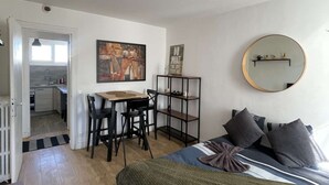 Une chambre à coucher avec un lit, un bureau, une chaise, un miroir et, au fond, une cuisine.